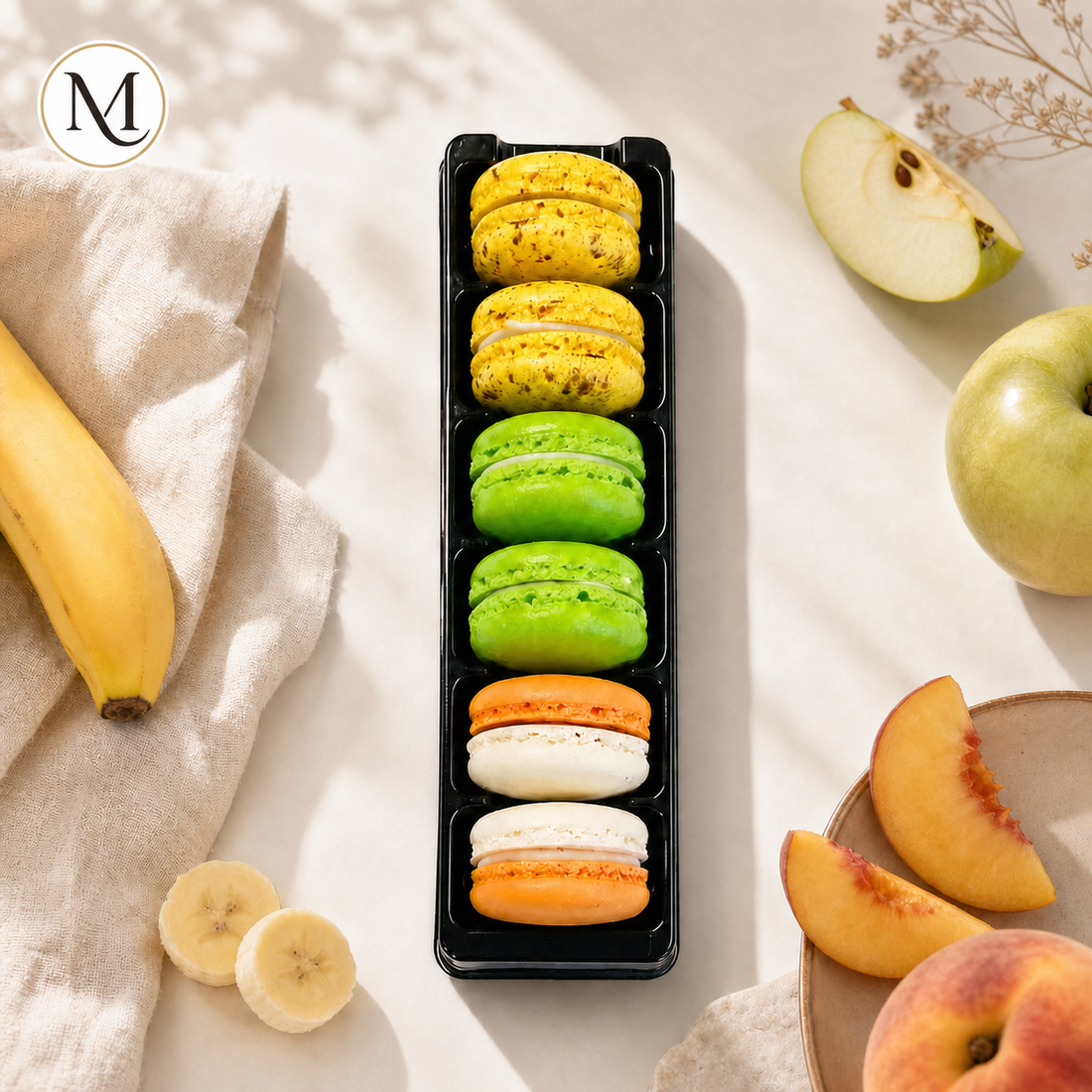 The Fruity Box van Macora met zes macarons in de smaken appel, banaan en perzik in een lichte zomerse setting.