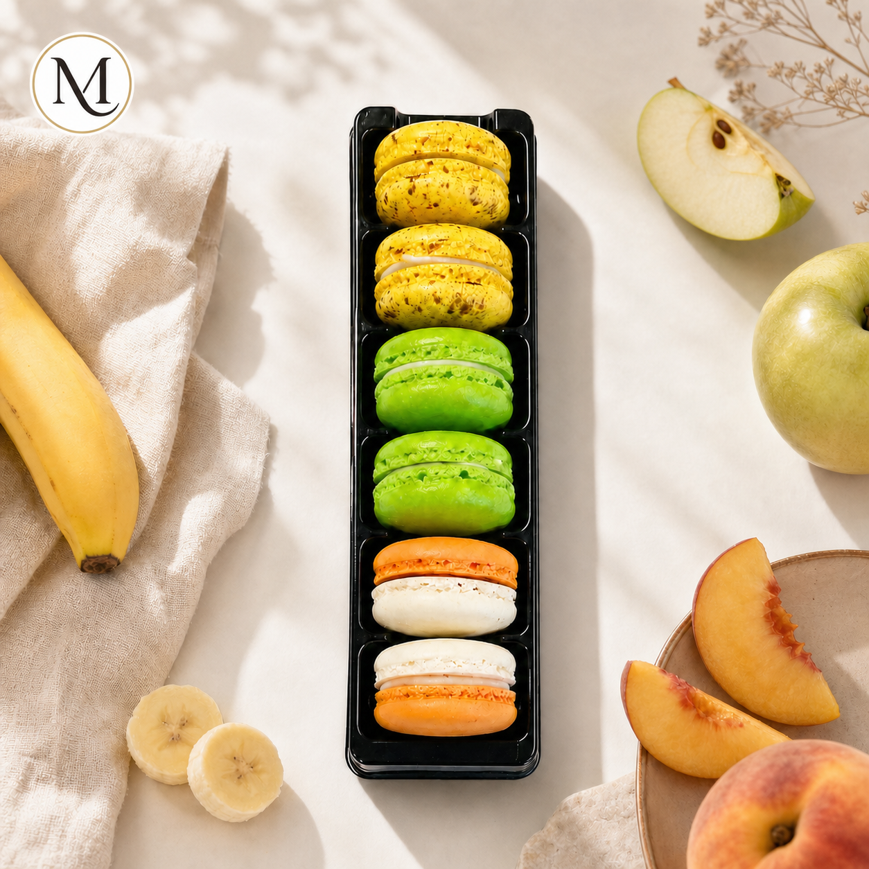 The Fruity Box van Macora met zes macarons in de smaken appel, banaan en perzik in een lichte zomerse setting.